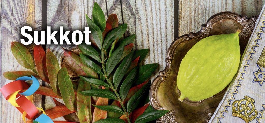 Etrog on an ornate plate with lulav leaves and colorful ribbons, a Sukkot-themed display.