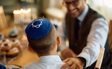 Back view of kid with yarmulke and his father at home during Hanukkah.